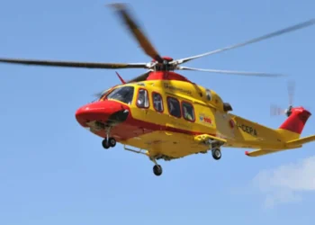 Elicottero del 118 giallo e rosso in volo su cielo azzurro, impiegato per il trasporto di un paziente in emergenza