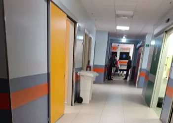 Corridoio dell'ospedale con un'ambulanza visibile all'ingresso e due persone sullo sfondo.
