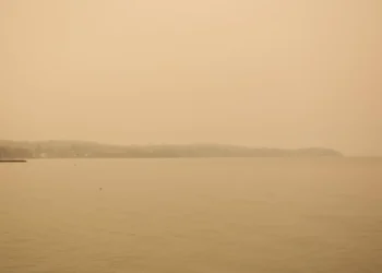 Cielo e mare avvolti da una foschia arancione di polvere sahariana, con la costa a malapena visibile all'orizzonte