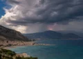 Temporale estivo sulla costa siciliana: nuvole scure, un fulmine sulle montagne e mare turchese in primo piano