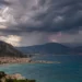 Temporale estivo sulla costa siciliana: nuvole scure, un fulmine sulle montagne e mare turchese in primo piano