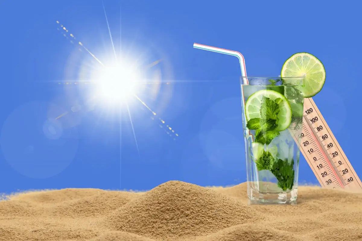 Sole intenso su spiaggia con bicchiere, lime, menta e termometro che segna temperature elevate