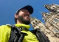 Antonio Giannone con zaino e bastoni sorride davanti alla cattedrale di Santiago de Compostela in una giornata di sole