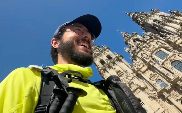 Antonio Giannone con zaino e bastoni sorride davanti alla cattedrale di Santiago de Compostela in una giornata di sole