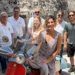Gloria Bortolini accanto a una Vespa d'epoca rossa e celeste, con i soci del Vespa Club Modica in un vicolo di Modica.
