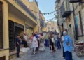 Gruppo di persone in una via del centro storico di Gangi, addobbata con nastri e spighe di grano per la festa estiva.