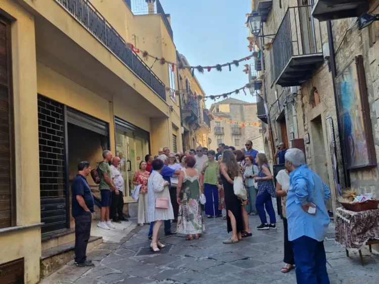 Gruppo di persone in una via del centro storico di Gangi, addobbata con nastri e spighe di grano per la festa estiva.