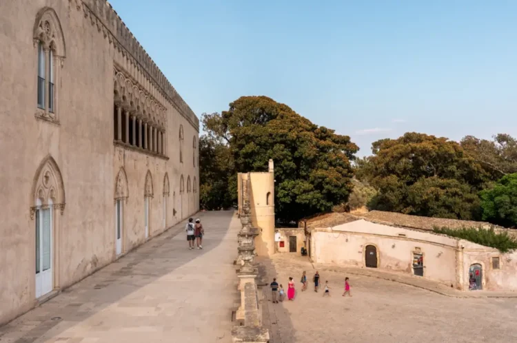 Visitatori nel cortile del Castello di Donnafugata a Ragusa, con la facciata neogotica e gli edifici rustici sullo sfondo