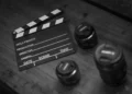 Ciak cinematografico in bianco e nero accanto a quattro obiettivi fotografici appoggiati su un tavolo di legno