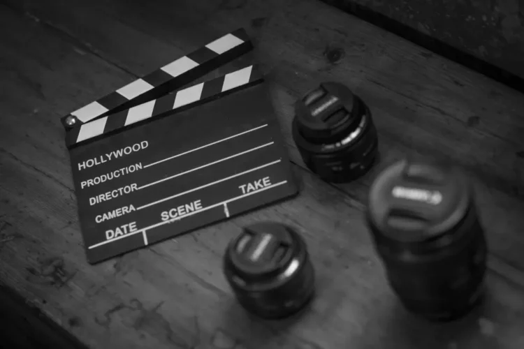 Ciak cinematografico in bianco e nero accanto a quattro obiettivi fotografici appoggiati su un tavolo di legno