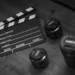 Ciak cinematografico in bianco e nero accanto a quattro obiettivi fotografici appoggiati su un tavolo di legno