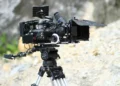 Macchina da presa professionale montata su treppiede durante una produzione cinematografica all'aperto.