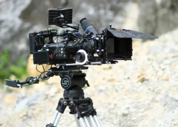 Macchina da presa professionale montata su treppiede durante una produzione cinematografica all'aperto.