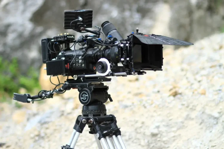 Macchina da presa professionale montata su treppiede durante una produzione cinematografica all'aperto.