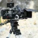 Macchina da presa professionale montata su treppiede durante una produzione cinematografica all'aperto.