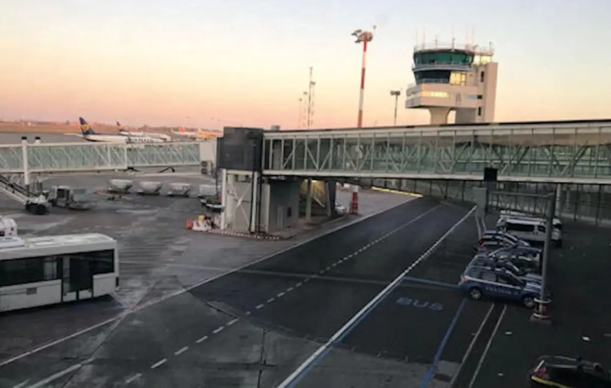 Pista dell'aeroporto di Catania-Fontanarossa con torre di controllo, aerei e passerella d'imbarco al tramonto