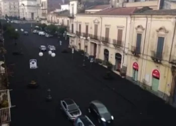 Strada del versante etneo ricoperta di cenere vulcanica scura, vista dall'alto, con auto in transito