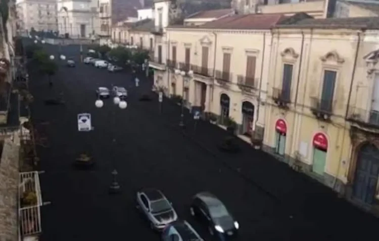 Strada del versante etneo ricoperta di cenere vulcanica scura, vista dall'alto, con auto in transito