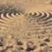 Cerchi concentrici tracciati nella sabbia chiara, visti dall'alto, con impronte intorno ai bordi