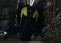 Scooter nero e giallo ripreso di notte su una strada urbana, con vegetazione sul lato destro e un'auto sullo sfondo