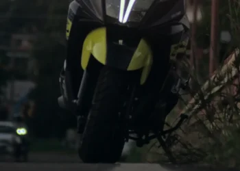 Scooter nero e giallo ripreso di notte su una strada urbana, con vegetazione sul lato destro e un'auto sullo sfondo