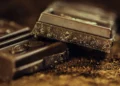 Tavolette di cioccolato fondente spezzate su polvere di cacao, con grana irregolare visibile sul bordo di frattura