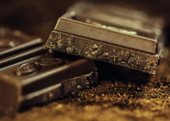 Tavolette di cioccolato fondente spezzate su polvere di cacao, con grana irregolare visibile sul bordo di frattura