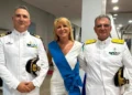 Una donna con fascia azzurra cerimoniale affiancata da due ufficiali in uniforme bianca della Guardia Costiera