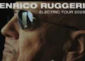 Primo piano di Enrico Ruggeri con occhiali da sole, locandina con scritta Electric Tour 2026.