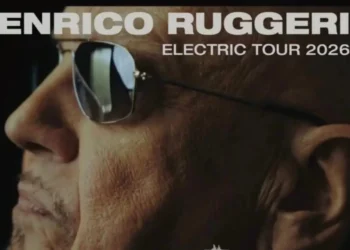 Primo piano di Enrico Ruggeri con occhiali da sole, locandina con scritta Electric Tour 2026.