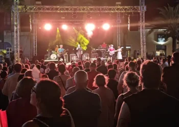 Il pubblico segue dal basso il concerto della band sul palco allestito in piazza, tra luci sceniche e palme.