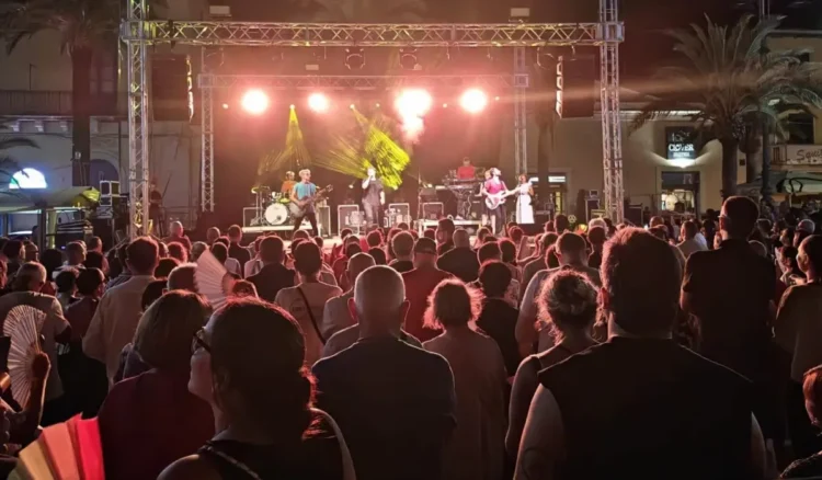 Il pubblico segue dal basso il concerto della band sul palco allestito in piazza, tra luci sceniche e palme.