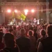 Il pubblico segue dal basso il concerto della band sul palco allestito in piazza, tra luci sceniche e palme.