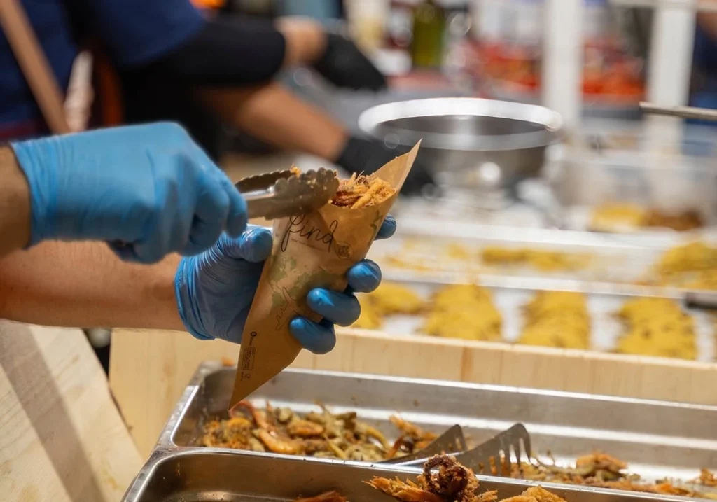 Operatore serve pesce fritto misto in un coppo di carta allo stand gastronomico della Sagra del Pesce di Pozzallo
