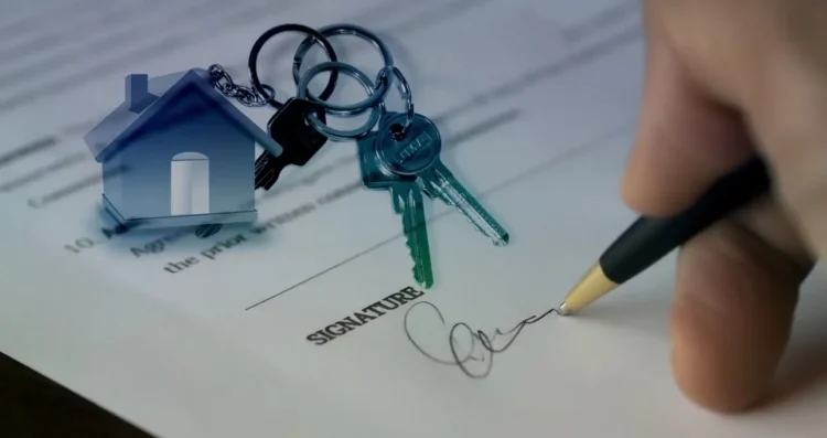 Una mano firma un contratto immobiliare, con un mazzo di chiavi e l'icona di una casa in sovraimpressione