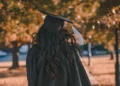 Persona in toga e tocco di laurea ripresa di spalle in un parco alberato