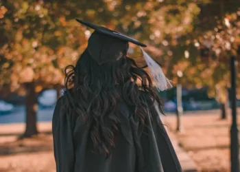 Persona in toga e tocco di laurea ripresa di spalle in un parco alberato