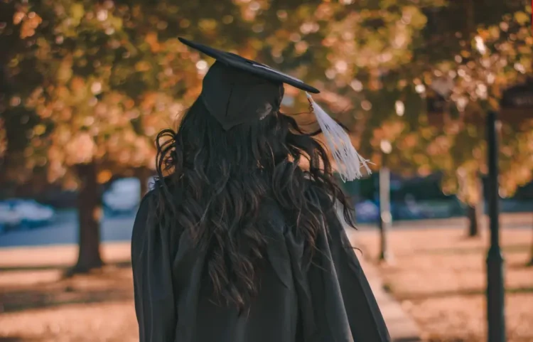 Persona in toga e tocco di laurea ripresa di spalle in un parco alberato