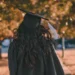 Persona in toga e tocco di laurea ripresa di spalle in un parco alberato
