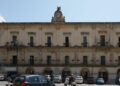 Palazzo comunale di Modica in stile barocco, con orologio in facciata, bandiera italiana e auto parcheggiate in piazza.