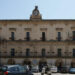 Palazzo comunale di Modica in stile barocco, con orologio in facciata, bandiera italiana e auto parcheggiate in piazza.