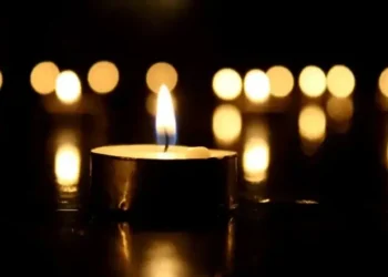 Una candela accesa in primo piano, con altre fiammelle sfocate sullo sfondo, su fondo scuro