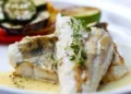 Filetto di pesce bianco grigliato con verdure di contorno e una fetta di lime, servito con salsa al burro e timo