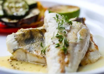 Filetto di pesce bianco grigliato con verdure di contorno e una fetta di lime, servito con salsa al burro e timo