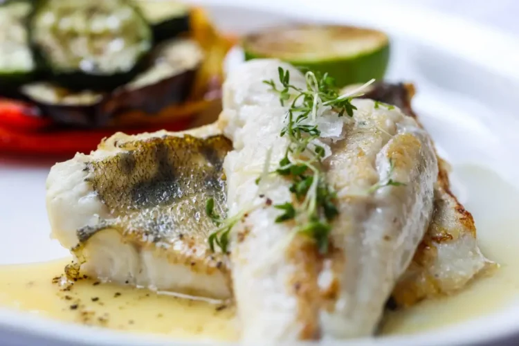 Filetto di pesce bianco grigliato con verdure di contorno e una fetta di lime, servito con salsa al burro e timo