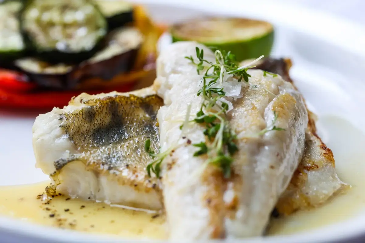 Filetto di pesce bianco grigliato con verdure di contorno e una fetta di lime, servito con salsa al burro e timo