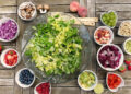 Insalatiera con verdure fresche e ciotoline di frutta, avocado, fragole e mirtilli su tavolo in legno