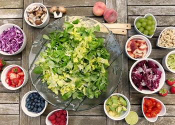 Insalatiera con verdure fresche e ciotoline di frutta, avocado, fragole e mirtilli su tavolo in legno