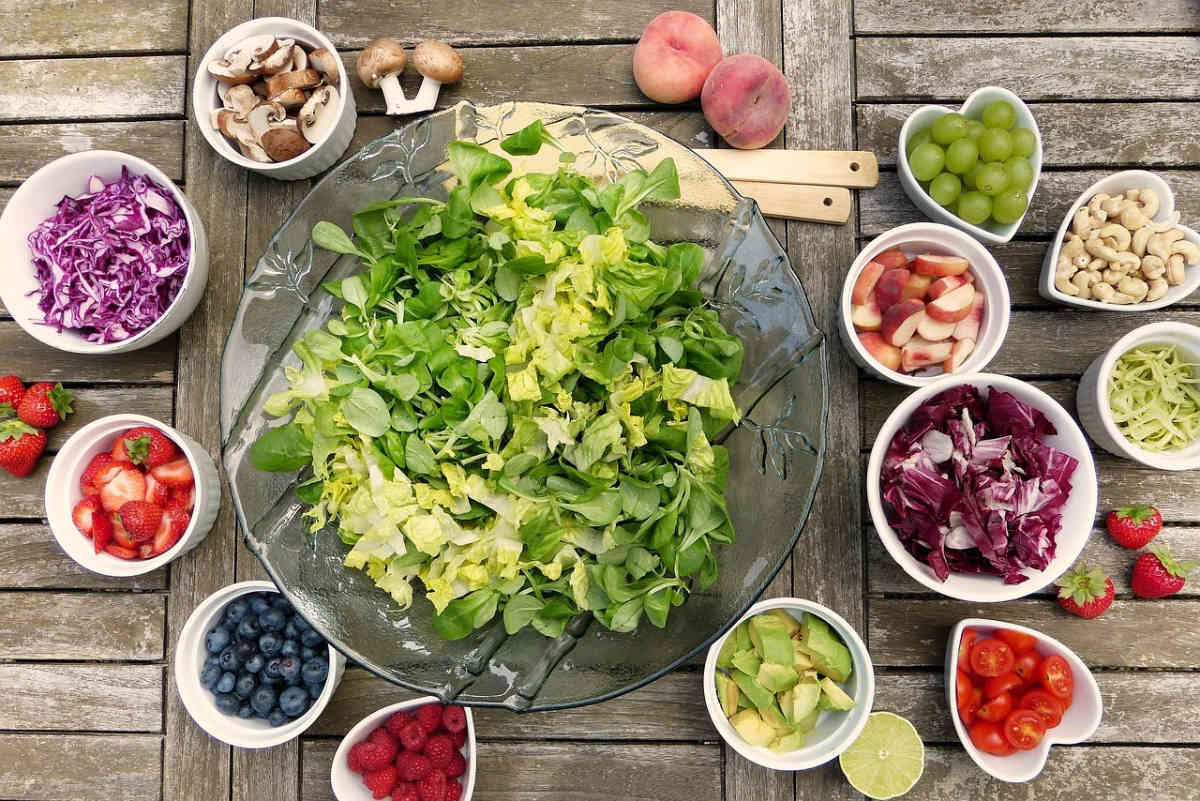 Insalatiera con verdure fresche e ciotoline di frutta, avocado, fragole e mirtilli su tavolo in legno