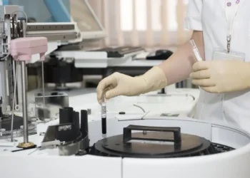 Mano guantata di un operatore sanitario preleva una provetta di sangue da un analizzatore automatico da laboratorio.